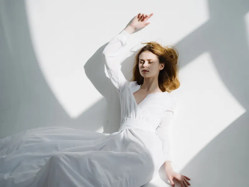 Рыжеволосая женщина в белом платье лежит на полу в лучах солнечного света