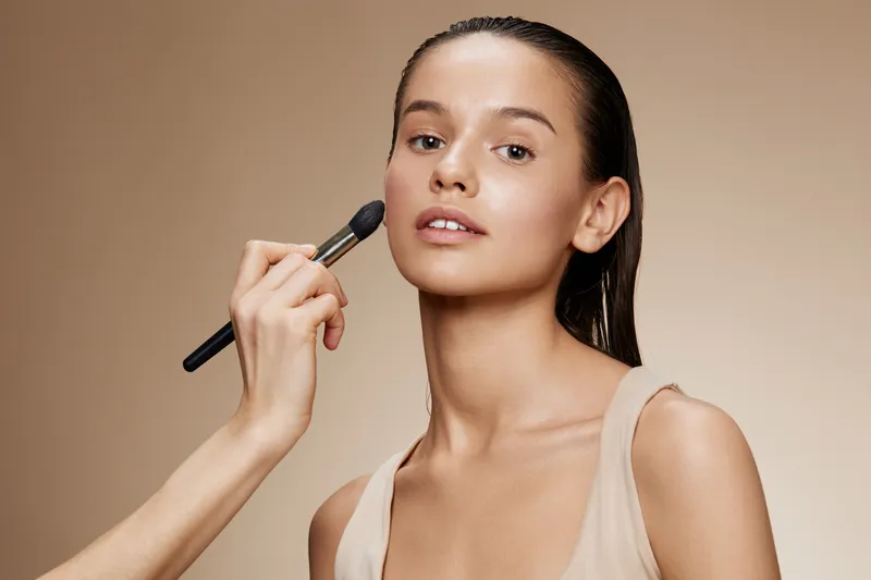 Young diverse model in natural makeup being applied, showcasing a healthy beauty vibe against a soft, neutral background Ideal for beauty and skincare promotions