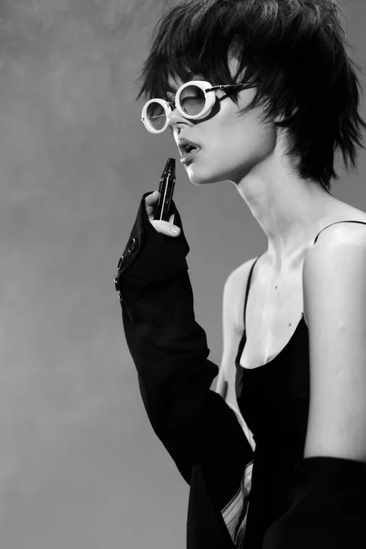 Black and white portrait of a stylish woman with short hair wearing sunglasses and a dark outfit in a minimalist setting