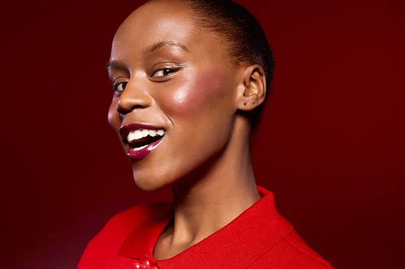 Portrait of smiling African American woman with dark skin and natural hair wearing red clothing on red background. Concept of beauty, confidence, fashion, and elegance in studio lighting.