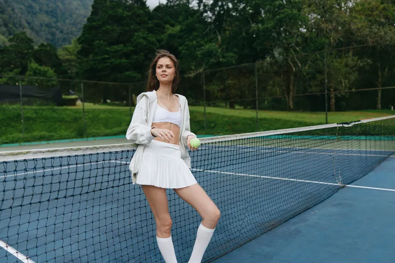 Young female athlete in stylish tennis outfit poses confidently on a court, showcasing sportswear, determination, and a vibrant outdoor environment