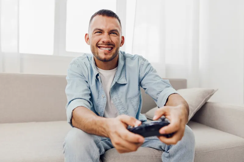 Happy man enjoying a gaming session, embracing technology and modern distractions, while reflecting on life's balance in a cozy living room setting.