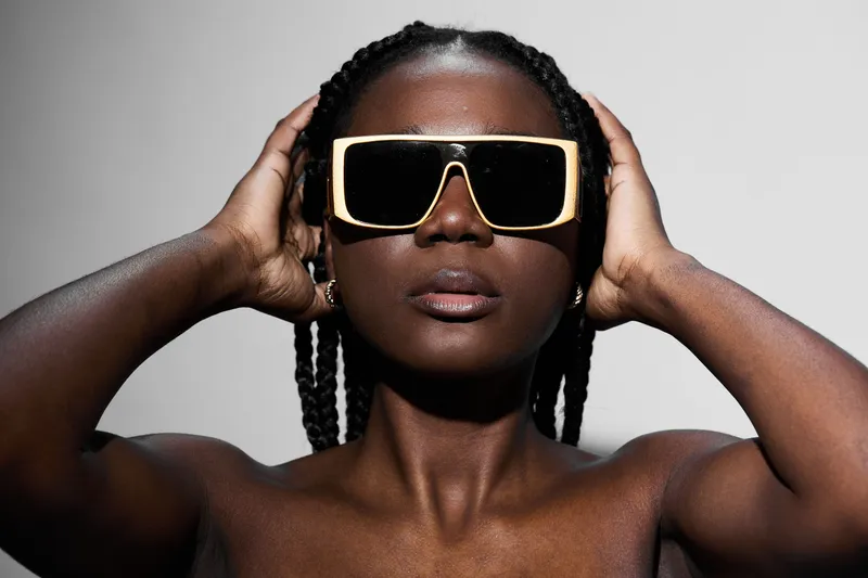 Confident woman with braided hair wearing oversized sunglasses, showcasing modern fashion and style against a minimalistic background