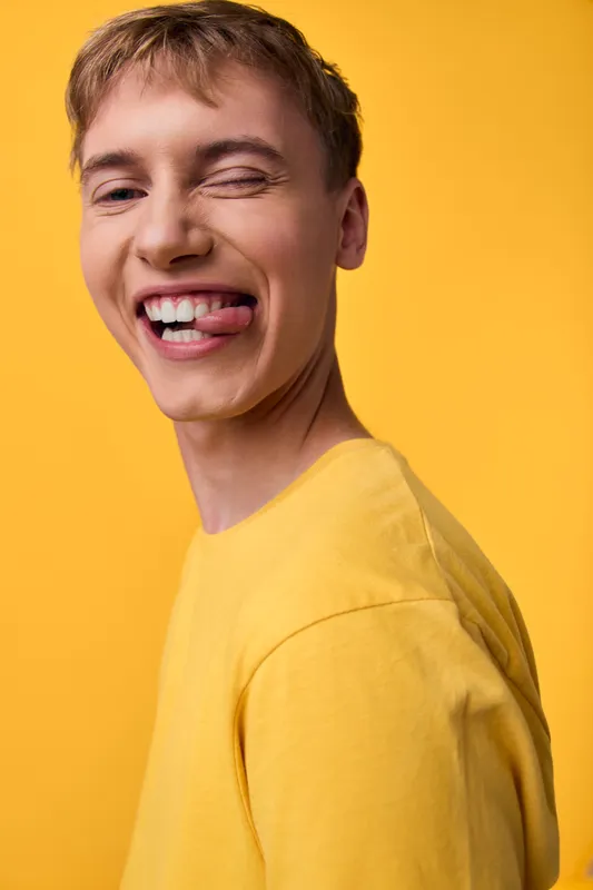 Joyful man in a yellow shirt against a solid yellow background, capturing a playful tongue out expression, bright studio mood, candid style for lifestyle, fashion, and upbeat branding projects