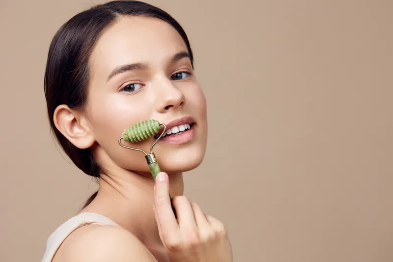 Young woman enjoying a facial roller treatment for healthy skin, showcasing a natural beauty routine with a soft, neutral background
