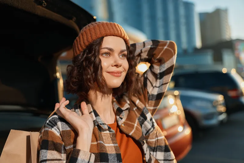 Woman portrait by an open car trunk, smile and beanie in golden hour sunshine. Candid lifestyle authenticity, mindful living and emotional storytelling with modern city warmth.