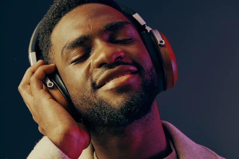A young man with headphones enjoying music, wearing a stylish jacket, displaying a joyful expression against a vibrant blue background Key elements include music, emotions, and lifestyle