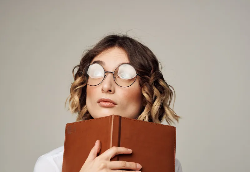 Женщина в очках держит в руке книгу на сером фоне