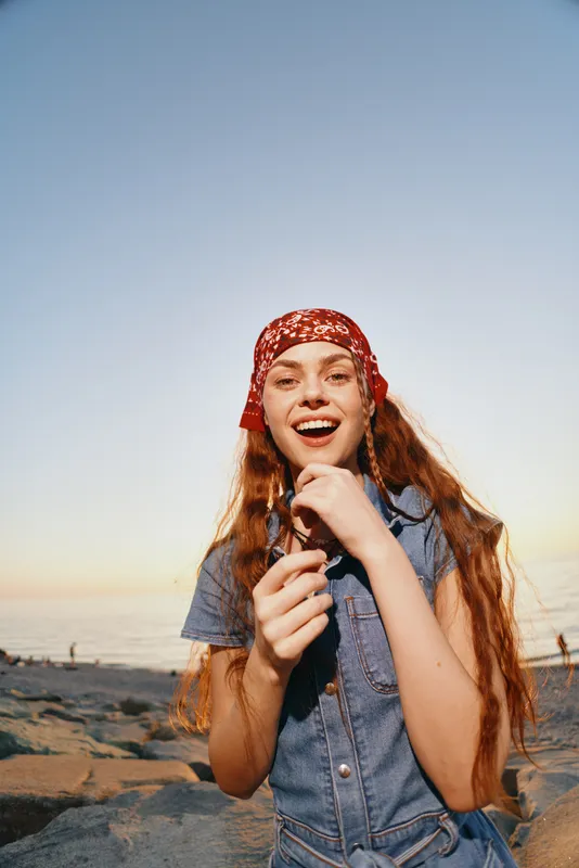 lifestyle woman in modern boho-western denim street style smiling outdoors with natural light and film color effect at sunset beach background