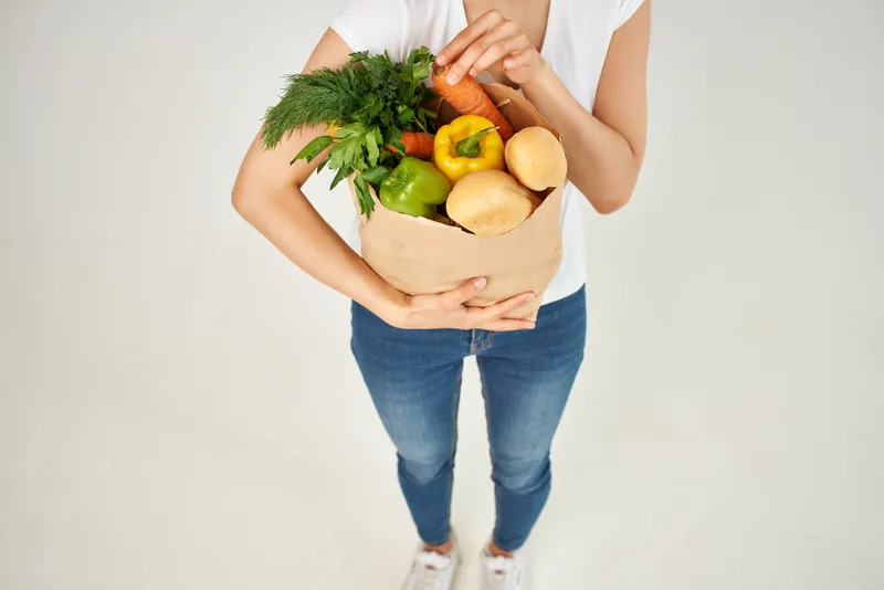 Женщина с пакетом продуктов, таких как овощи, в супермаркете, обрезанный вид