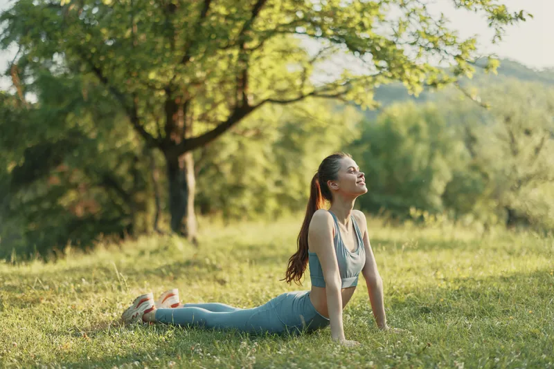 Young fitness woman practicing yoga in a serene green park during summer, enjoying a moment of peace and wellness while stretching