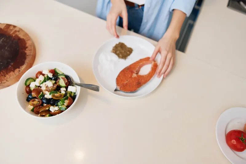 Женщина готовит вкусное и полезное блюдо из свежих овощей и лосося на кухонной стойке