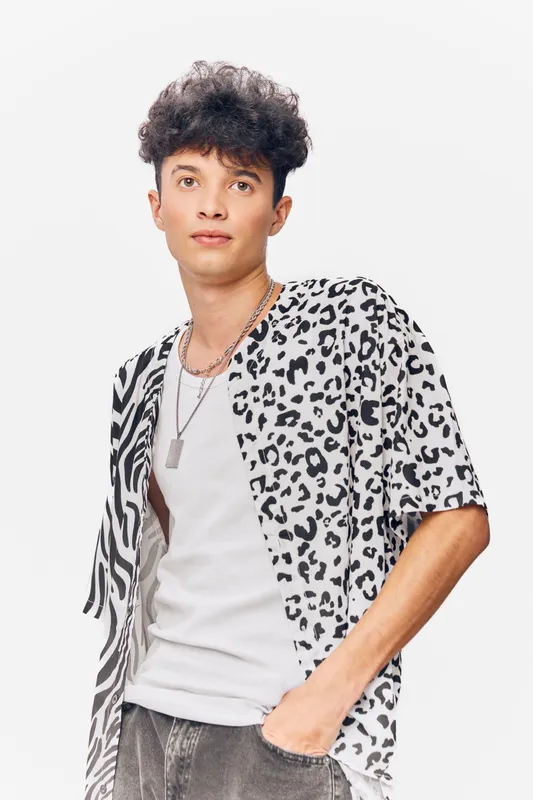 young man wearing a half leopard print shirt with curly hair and neutral expression posing against a bright white background in casual style