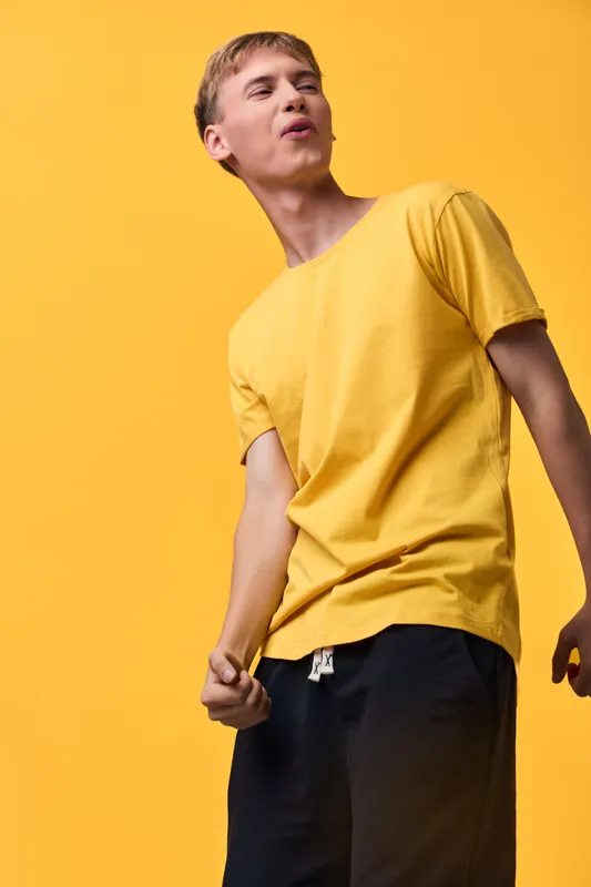 Energetic man in a bright yellow shirt strikes a dynamic pose before a bold yellow backdrop, conveying casual fashion, vivid color, motion, and confident expression, with a bright studio feel and