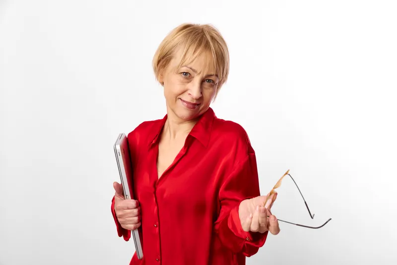 Senior woman in red shirt holding smartphone and glasses, smiling softly, using technology for communication and learning, studio background, lifestyle concept