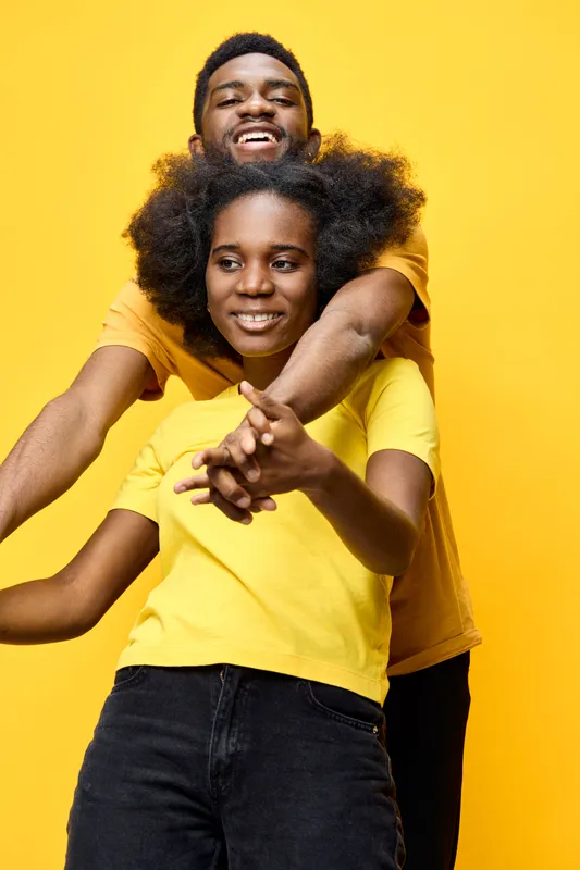 Happy multicultural couple in bright yellow t shirts laughing together against a vibrant yellow background, expressing joy and love