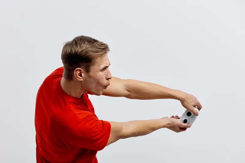 Young caucasian man playing video game with controller in red t-shirt isolated on white background focus concentration digital entertainment concept