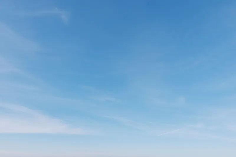 Blue sky with light wispy clouds over a calm horizon, open space for sunlight and air, ideal background for nature, travel, or inspirational projects.