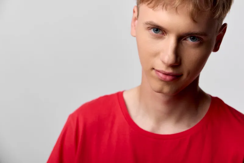 Young man, red shirt, close up, studio lighting, thoughtful expression, casual attire for fashion and lifestyle shoot, clean background, soft tones, modern look, minimal distraction