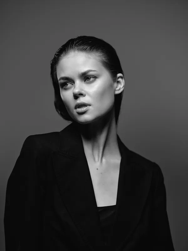 Black and white portrait of a young woman in a dark blazer with serious expression and slicked-back hair.