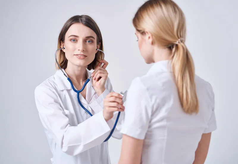 Врач в медицинском халате на светлом фоне и пациентка — блондинка