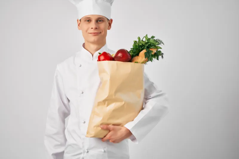 Мужчина в поварской форме с пакетом продуктов работает в сфере обслуживания ресторана
