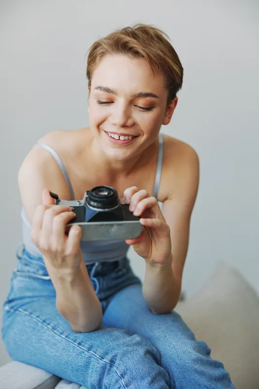 Женщина-фотограф снимает в студии на старую плёночную камеру, сидя на диване дома, портрет на белом фоне, свободное место для копирайтинга, фриланс-фотограф