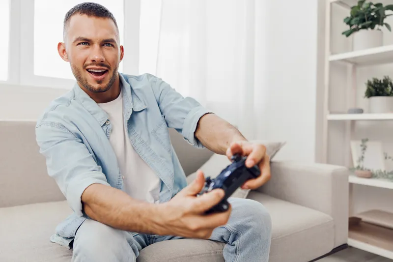 Excited man enjoying video games indoors, showcasing enthusiasm and focus while playing. Ideal for contemporary themes in technology and leisure activities.