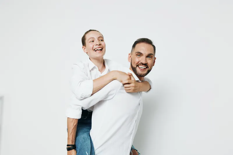 A confident businessman smiles as a colleague piggybacks on his shoulders, showcasing teamwork, energy, and positive emotion against an isolated white background.