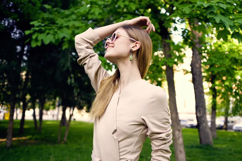 Симпатичная женщина в солнцезащитных очках на прогулке среди зелёных деревьев в парке