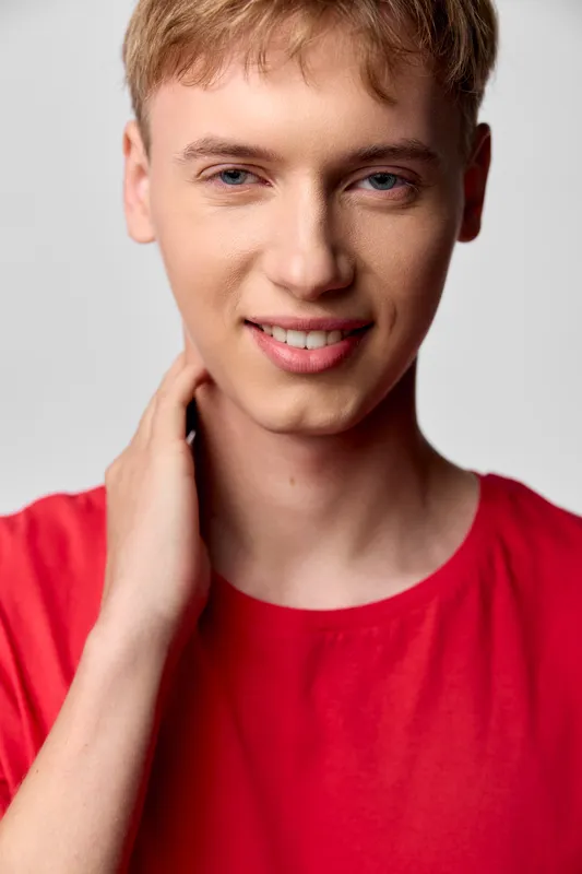 Young man with a warm smile in a red shirt in a studio setting, clean background, upbeat casual headshot for lifestyle, fashion and wellness concepts