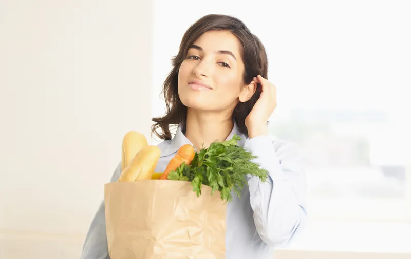 Брюнетка с пакетом продуктов, включающим овощи и зелень, совершающая покупки в супермаркете