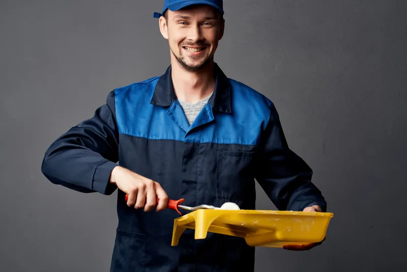 Маляр-мужчина с валиком выполняет покрасочные работы в комнате