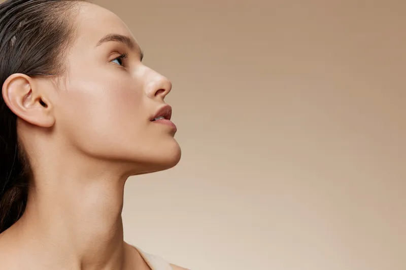 Elegant profile portrait of a young woman with smooth skin and natural beauty against a soft beige background, conveying confidence and serenity