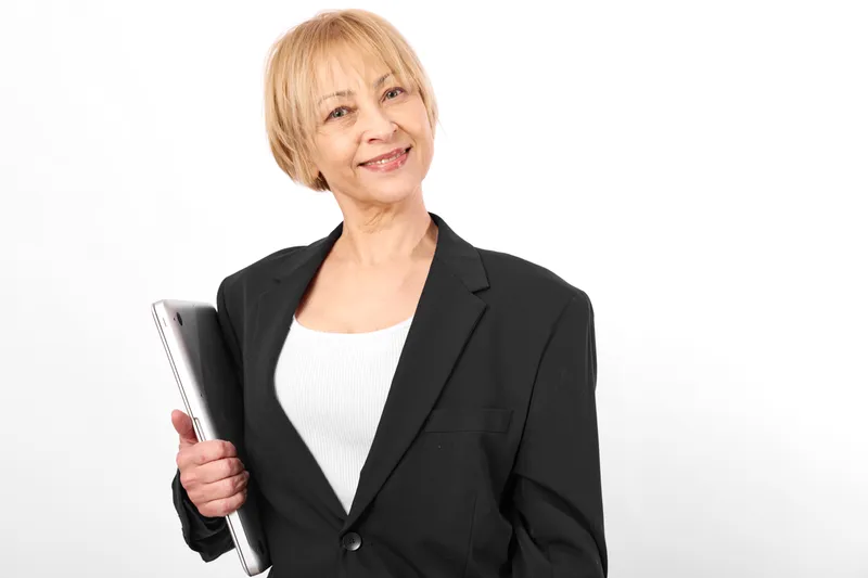 Elderly woman in black blazer holding a tablet, smiling confidently, bright studio background, relaxed posture, modern technology, business portrait, soft even light clean