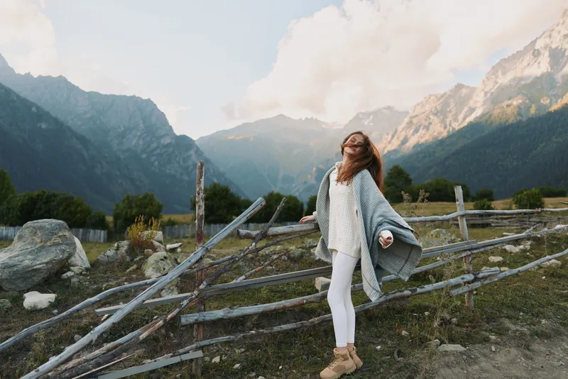 Cheerful woman outdoors, enjoying mountains, scenery, casual outfit, flowing cardigan, sunlit air, relaxed pose, natural colors, alpine landscape, carefree mood