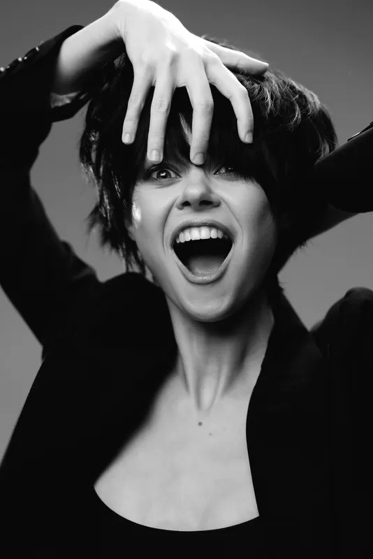 Black and white portrait of an excited woman with short hair expressing joy and surprise in a studio setting.