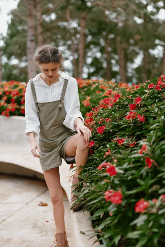 Young woman in a stylish summer outfit, gracefully posing among vibrant flowering plants in a garden setting Emphasizes seasonal beauty and fashion