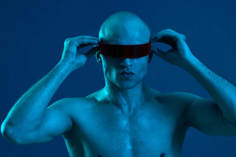 A modern man with a futuristic look, showcasing unique eyewear in a monochromatic blue ambiance. Ideal for tech-themed visual projects.