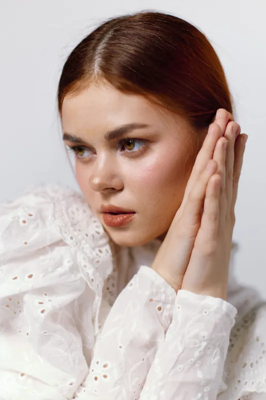 Young woman with long hair in a white shirt expressing calmness and serenity, captured in a minimalist background emphasizing soft tones