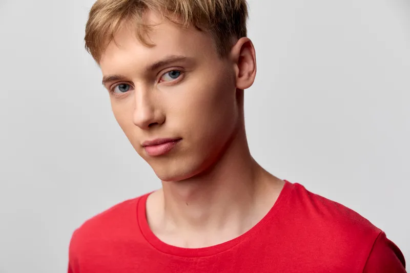 Close up of a young man with short blond hair wearing a red shirt, looking at the camera with a calm expression, studio lighting and a clean background, minimal style and natural color tones.
