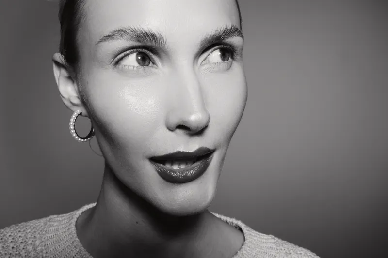 Close-up black and white portrait of a young white woman with light skin wearing hoop earrings and a sweater. Concept for fashion, beauty, and minimalistic style photography.