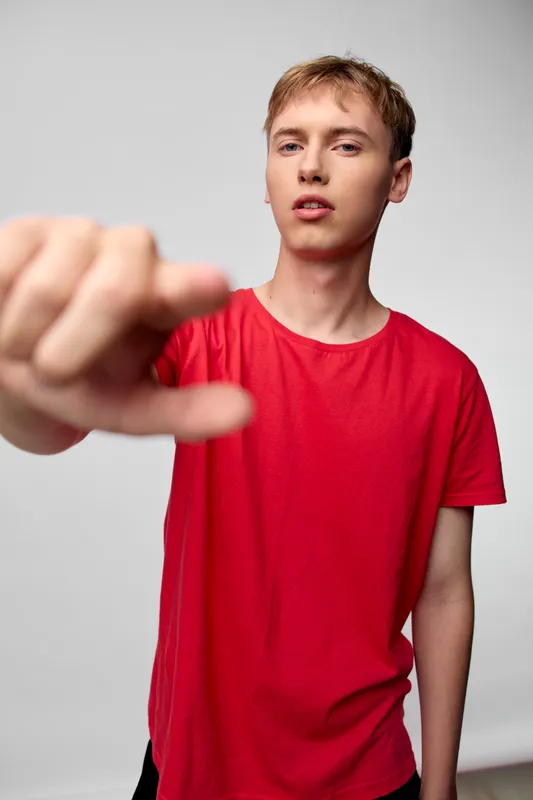 Dynamic closeup of a young man in a red shirt reaching toward the camera, action pose, energetic mood, bold perspective in a studio setting.
