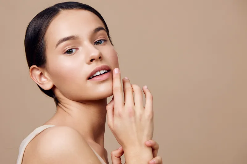 Young woman with natural beauty touching her face, showcasing glowing skin and a serene expression, ideal for wellness and skincare concepts