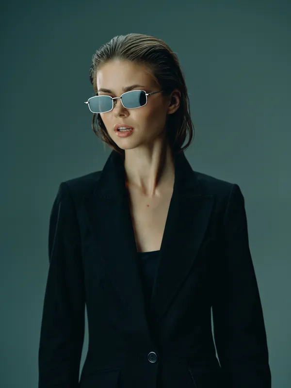 Stylish woman wearing sunglasses and black blazer with confident expression in studio lighting