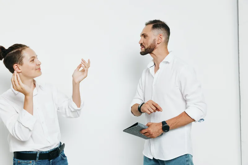 Two professionals, a man and a woman, stand against an isolated solid color backdrop, sharing a thoughtful moment as they discuss strategy with confident, poised gestures.