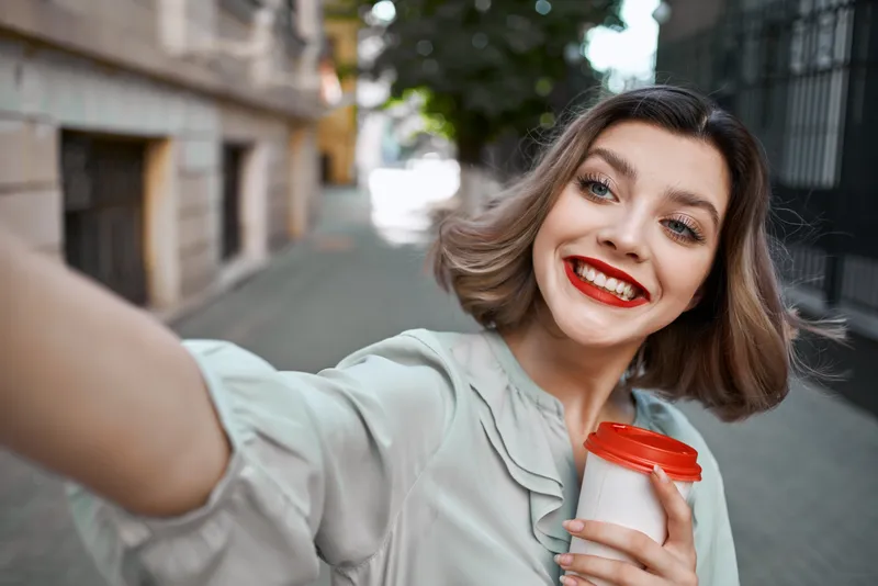 Жизнерадостная блондинка с чашкой кофе на улице, стиль жизни