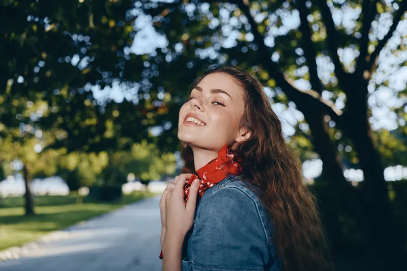 Lifestyle woman in modern boho-western denim street style smiling outdoors with natural sunlight and vibrant film color creating a relaxed and stylish mood.