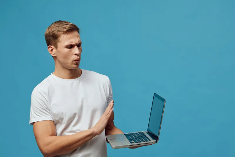 surprised man holding laptop in white t-shirt isolated on blue background digital nomad remote work concept