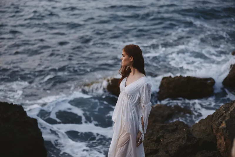 Женщина в белом платье на фоне природы: летний каменистый утёс на побережье